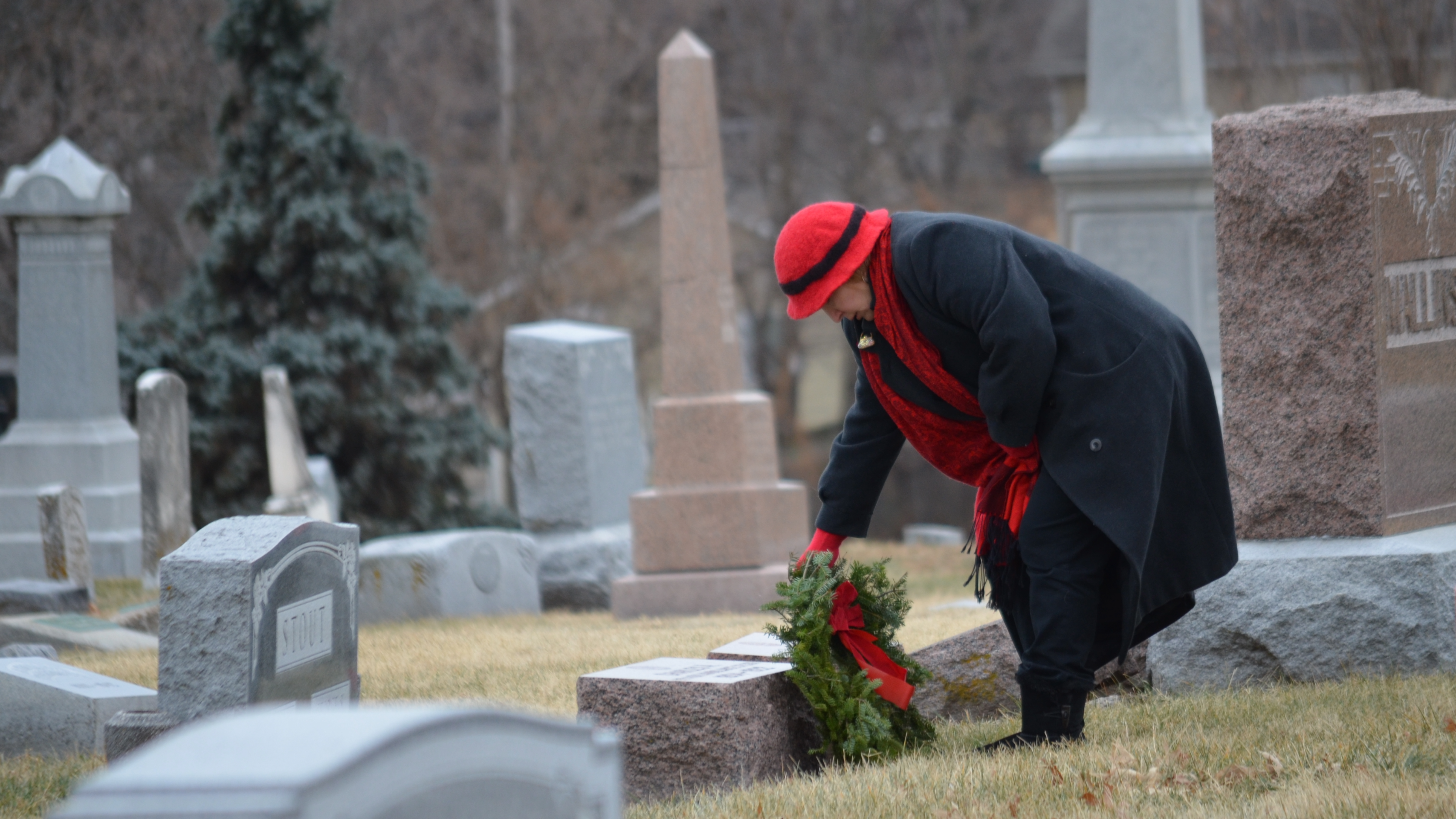 Image of a woman placing a wreath on the grave of a service member at Woodlawn Cemetery
