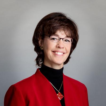 A portrait of Councilmember McCandless in a red suit jacket, black turtleneck, and red necklace.
