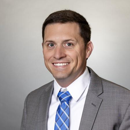 A portrait of City Manager Zach Walker in a light grey suit with a white shirt and blue tie. 