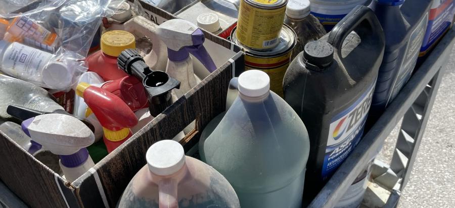 A cart filled with old paint and other household hazardous waste items sits in the sunshine in a parking lot waiting to be disposed of safely. 