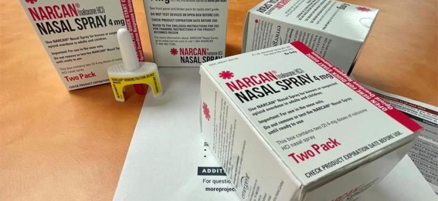 A box of Narcan, a small white bottle with a yellow base, sits on top of a pile of papers discussing drug addiction and treatment options