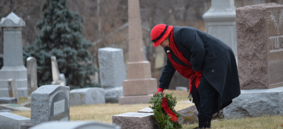 Image of a woman placing a wreath on the grave of a service member at Woodlawn Cemetery