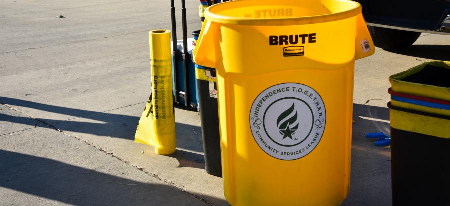 A bright yellow trash can with a green and white sticker on the front that reads Independence TOGETHER 