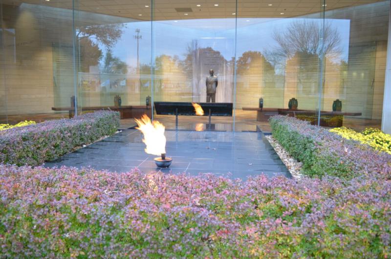 Eternal Flame burning in the courtyard of the Harry S. Truman Library and Museum in the foreground. A statue of Truman is in the background. 