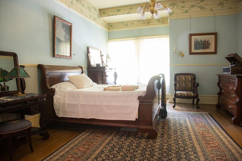 Image of a bedroom in the Bingham-Waggoner Estate with a bed on the left, dresser in the background, and a dresser on the right.
