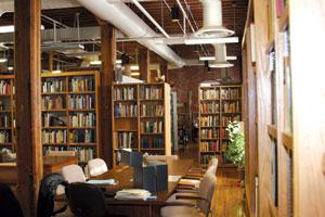 Inside image of the Merril Library. Bookshelves with books and seating in the foreground center. 