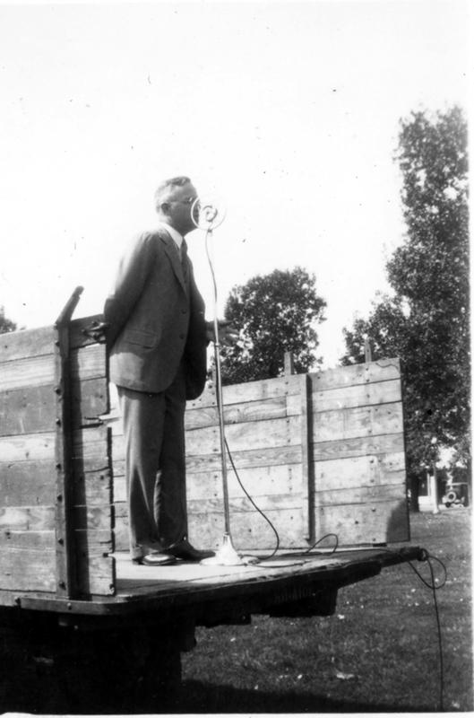 Judge Harry S. Truman at Sikeston, speaking through a microphone as he stands on the back of a truck bed.