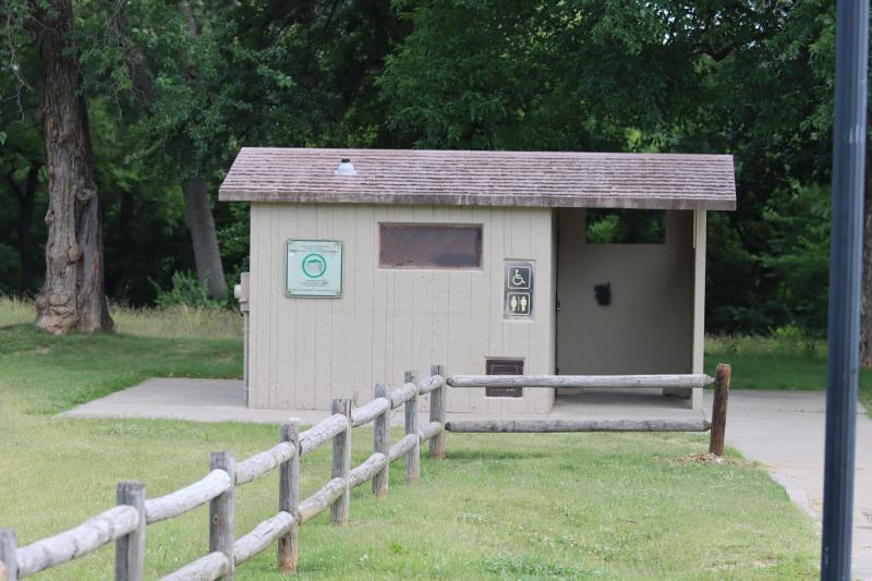 An image of the restroom outside structure at Dickinson Park with a wooden fence next to it.