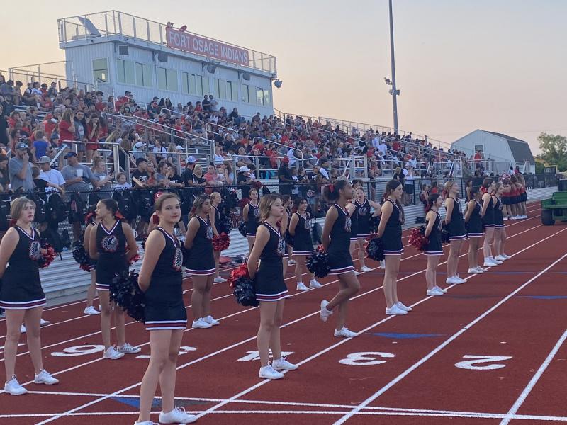Cheerleaders from the Fort Osage High School stand in front of spectators at a sporting event in the Fort Osage High School Football stadium.