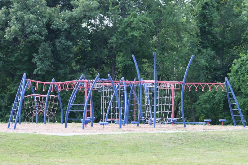 An image of a red and blue playground with rope climbing equipment at the Independence Athletic Complex. Trees are sitting in the background.