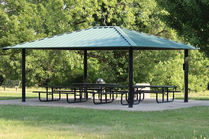 An image of the Bundschu Park shelter with picnic tables and trees in the background.