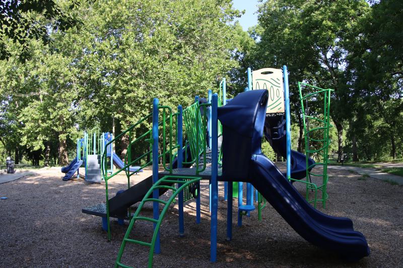 An image of one bigger blue and green colored playground and a smaller blue and green colored playground at Fairmount Park shaded by some trees.