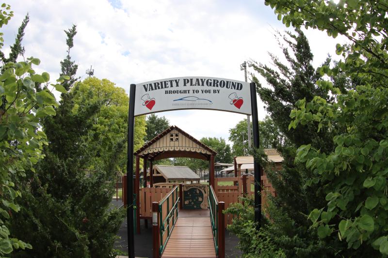 An image of the entrance to the inclusive playground at McCoy Park with a banner that reads 'variety playground' surrounded by trees and landscaping.