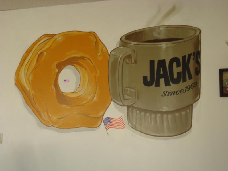 A picture of a donut resting near a coffee mug with the Jacks Donuts text