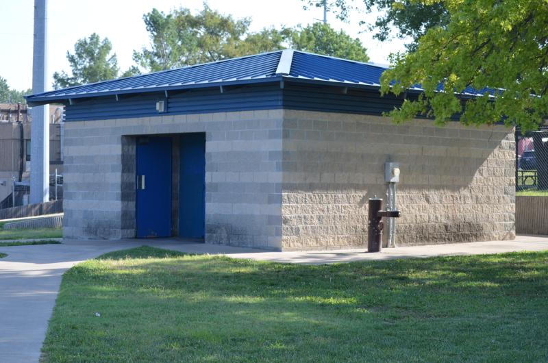 An image of the men's and women's restroom structure surrounded by a sidewalk and a water fountain on one side at McCoy Park.