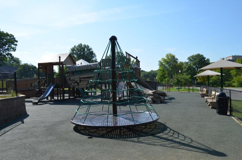 An image of different play equipment inside the fenced playground area at McCoy Park with a few benches on the side for seating.