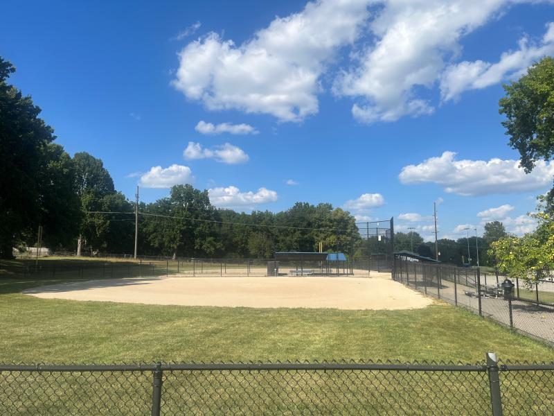 An image of a smaller dirt baseball field at Mill Creek Park on a partly cloudy day.