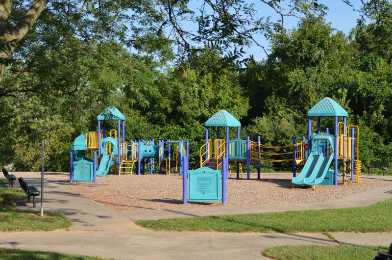 An image of a blue and yellow playground area surrounded by a sidewalk and two benches at Santa Fe Park.