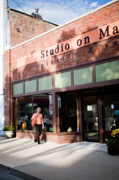 The exterior of Studio on Main, a pilates and yogo studio in Independence.The image shows the exterior wall with a woman walking by on the sidewalk