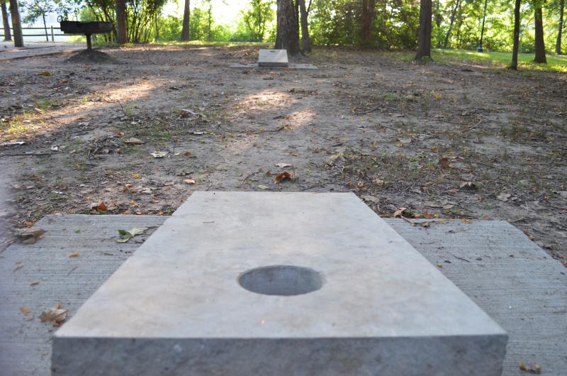 A close-up image of a concrete cornhole board and in the distance the other concrete cornhole board among the trees at Waterfall Park.