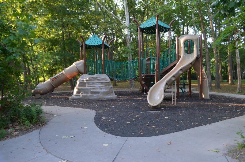 An image of a beige and green playground surrounded by a sidewalk and trees at Waterfall Park.