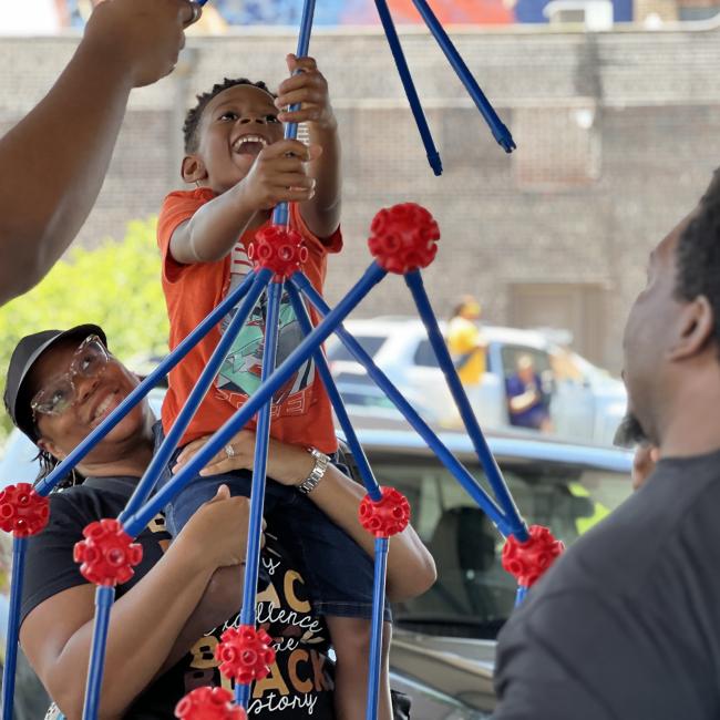 A mother lifts her child building with large scale toys at the Juneteenth event in 2023.