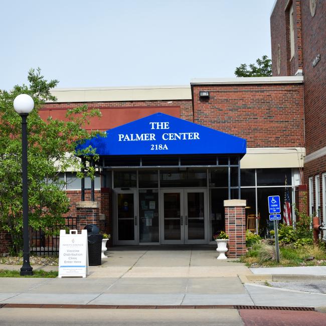 A blue awning sits over the front door of the Palmer Senior Center. It has white words with The Palmer Center 218A printed on it.