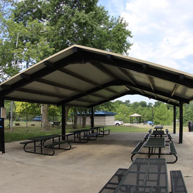 A close up image of the McCoy Park pavilion structure with seven picnic  tables and trees in the background.