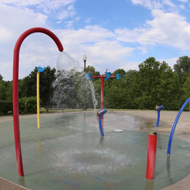 An image of McCoy Park water playground with water coming out of splash pad features on a partly cloudy day.