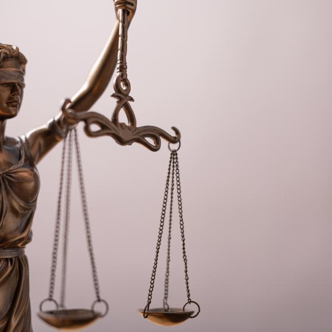 A statuette of Lady Justice holds the scales in front of a grey background. 