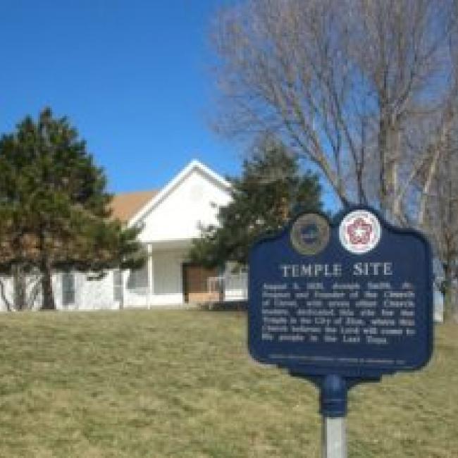 An exterior view of the site where the original temple lot dedicated by Joseph Smith is located. Picture includes a building and historic marker.