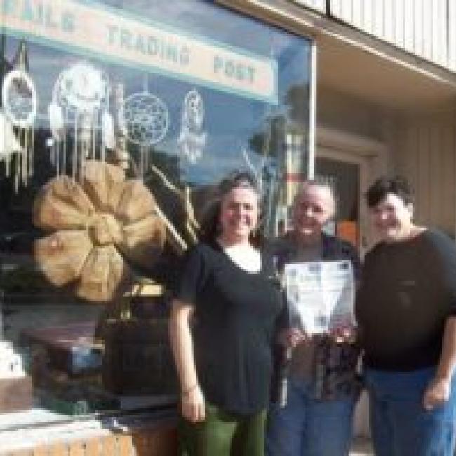 The exterior of Three Trails Trading Post with three people standing in front smiling
