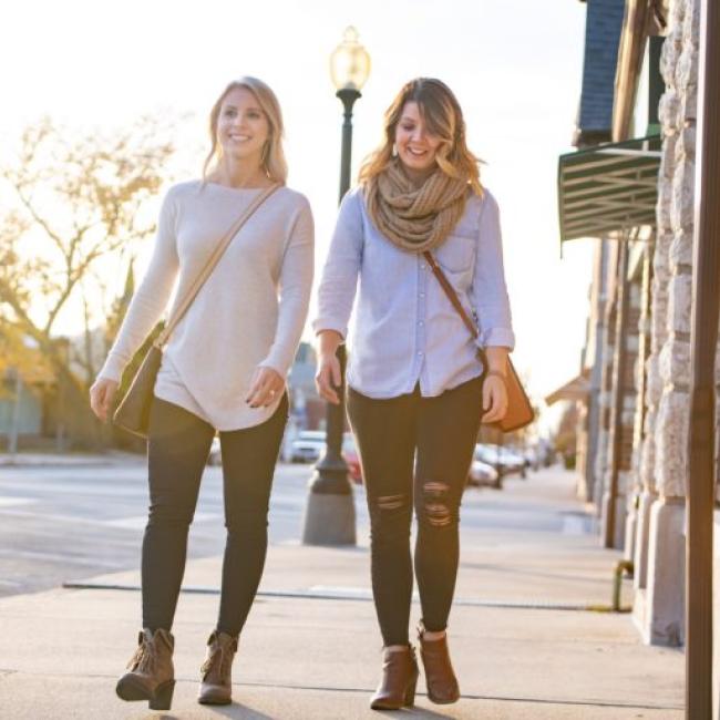 two women in long sleeved shirts walk down a sidewalk on a fall day in downtown Independence